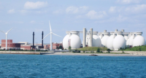 White water storage tanks sit beside wind turbines on a riverfront.