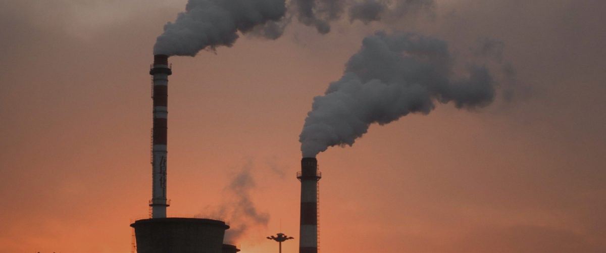 Smokestacks rise in front of an orange sky