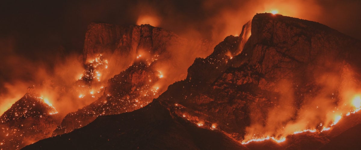 Flames and orange smoke shroud a black mountain range.