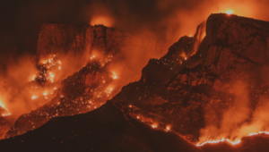 Flames and orange smoke shroud a black mountain range.