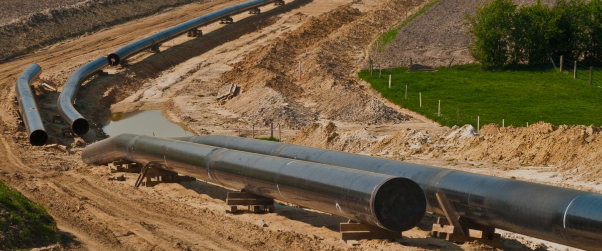A pipeline in progress lies on brown earth, cutting through green grass.