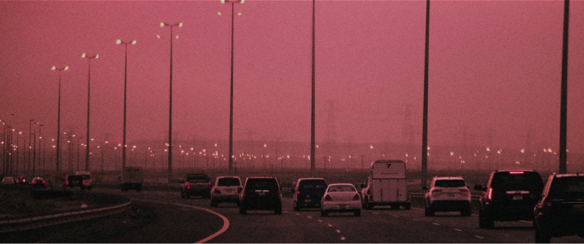 Cars on a highway blanketed in hazy pollution and a pink sky.