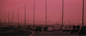 Cars on a highway blanketed in hazy pollution and a pink sky.