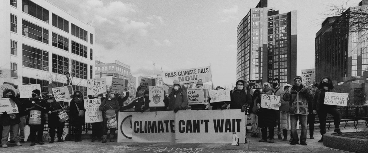 In black and white, a group of protestors holds signs in front of three tall buildings.