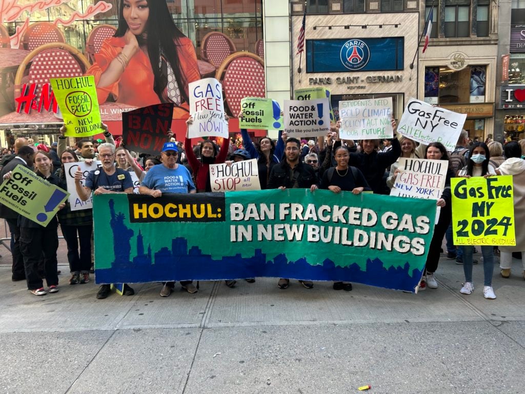At a rally, a line of activists stand with signs and a banner reading: "HOCHUL: BAN FRACKED GAS IN NEW BUILDINGS."
