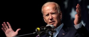 President Biden stands in front of a microphone with his hands outstretched.