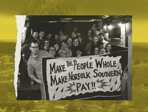 A crowd of organizers stand together with a banner that reads, "Make the people whole, make Norfolk Southern pay!!"