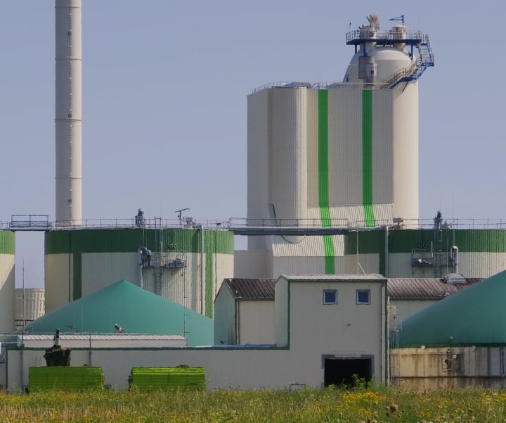 A digester facility, which turns waste into factory farm gas, sits on a patch of grass, with white towers and lower green-domed buildings.