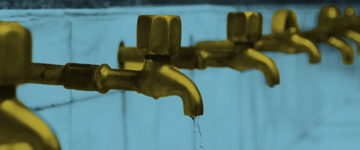 Several faucets stick out from tiled wall in a line.