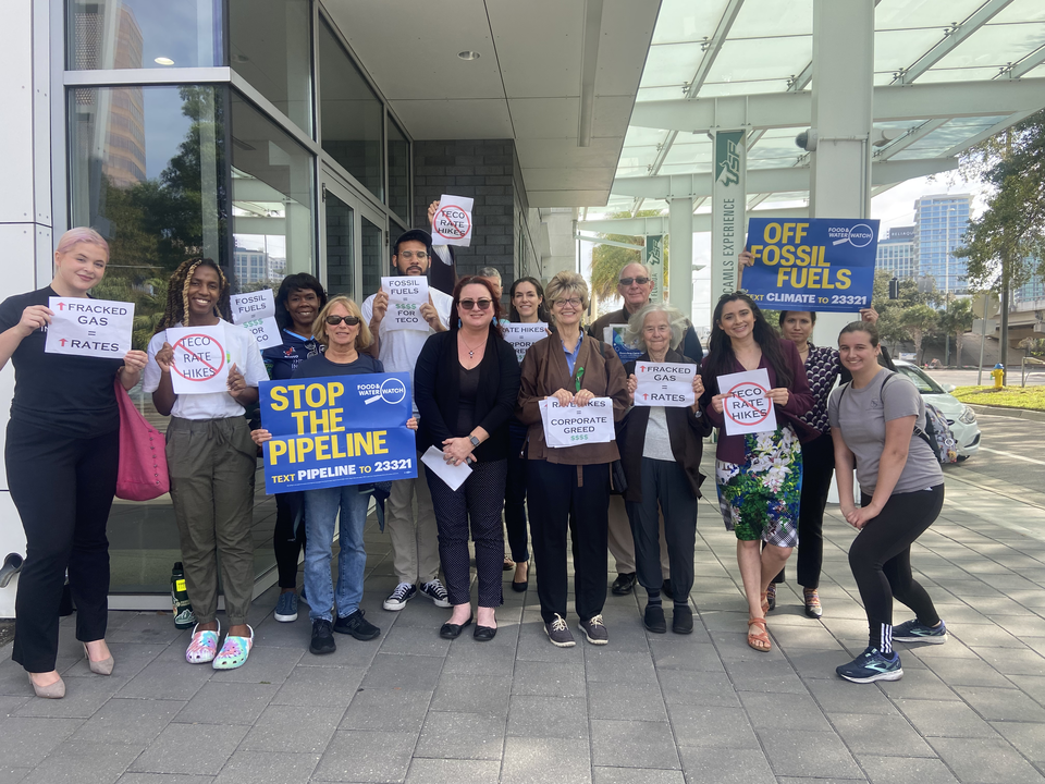 A group of advocates stand with signs that read "More fracked gas = higher rates," "Stop the pipeline," "Off fossil fuels," and "TECO RATE HIKES" with a red circle and slash over it.