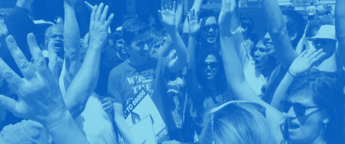 A crowd at a rally smile and shout with their hands in the air.