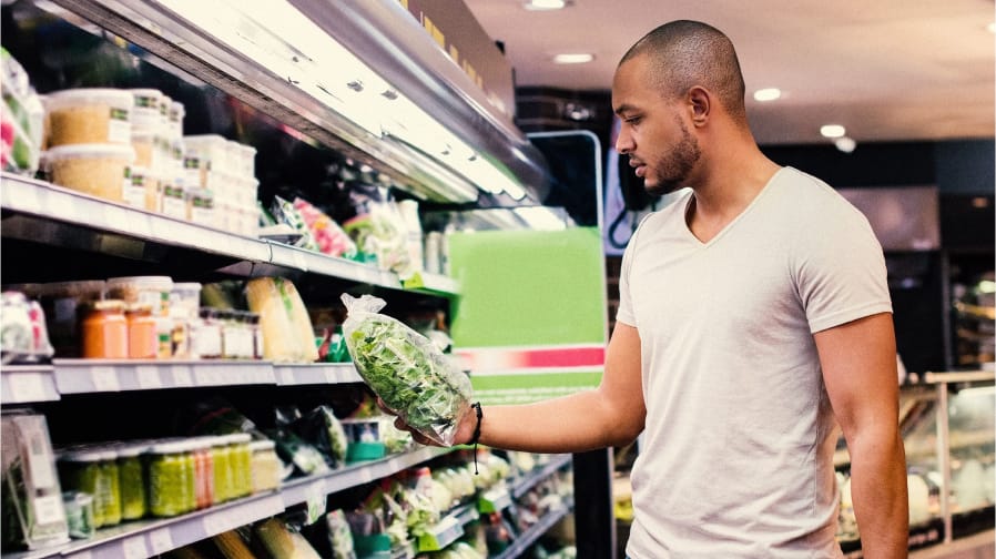 A color photo of a black man examining a package of greens at the grocery store. Big Ag is Draining the Colorado River Dry