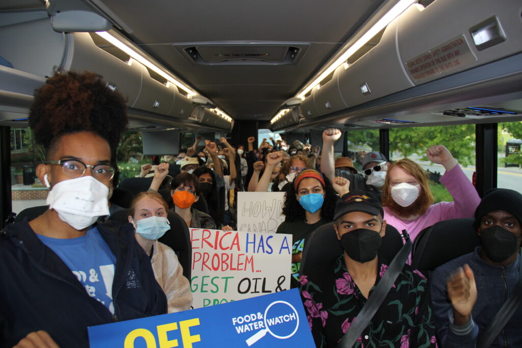 Young people sit in a coach bus wearing surgical masks and holding protest signs. Several have their fists raised in a sign of solidarity and power.