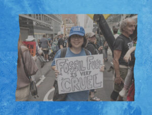 Climate activist Kaitlyn Quach stands amid a busy New York City street wearing a blue baseball cap and holding a sign that says, "Fossil fuel is very cruel."