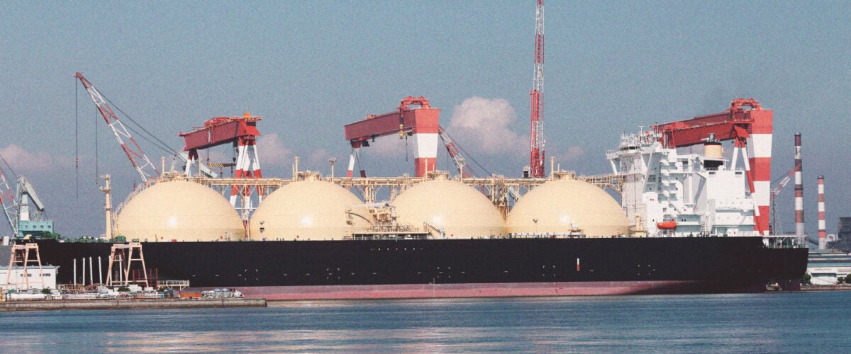 An massive LNG ship with its round half-sphere tanks sits on blue water.