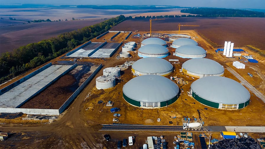 An aerial shot of eight round, domed digesters beside long, rectangular open-air manure.