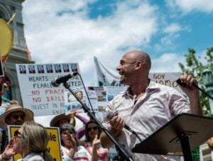 David Braun stands with a crowd behind him and a podium in front of him, looking to his right and slightly behind, smiling.