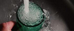 A stream of water falls into a green glass cup.