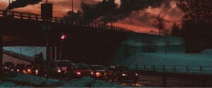 Cars drive past smoke stacks chugging pollution into the air.