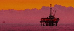 Big Oil Wants to Turn Our Oceans Into Its Dumping Grounds. A pink and orange tinted background horizon and a view of an ocean oil rig.