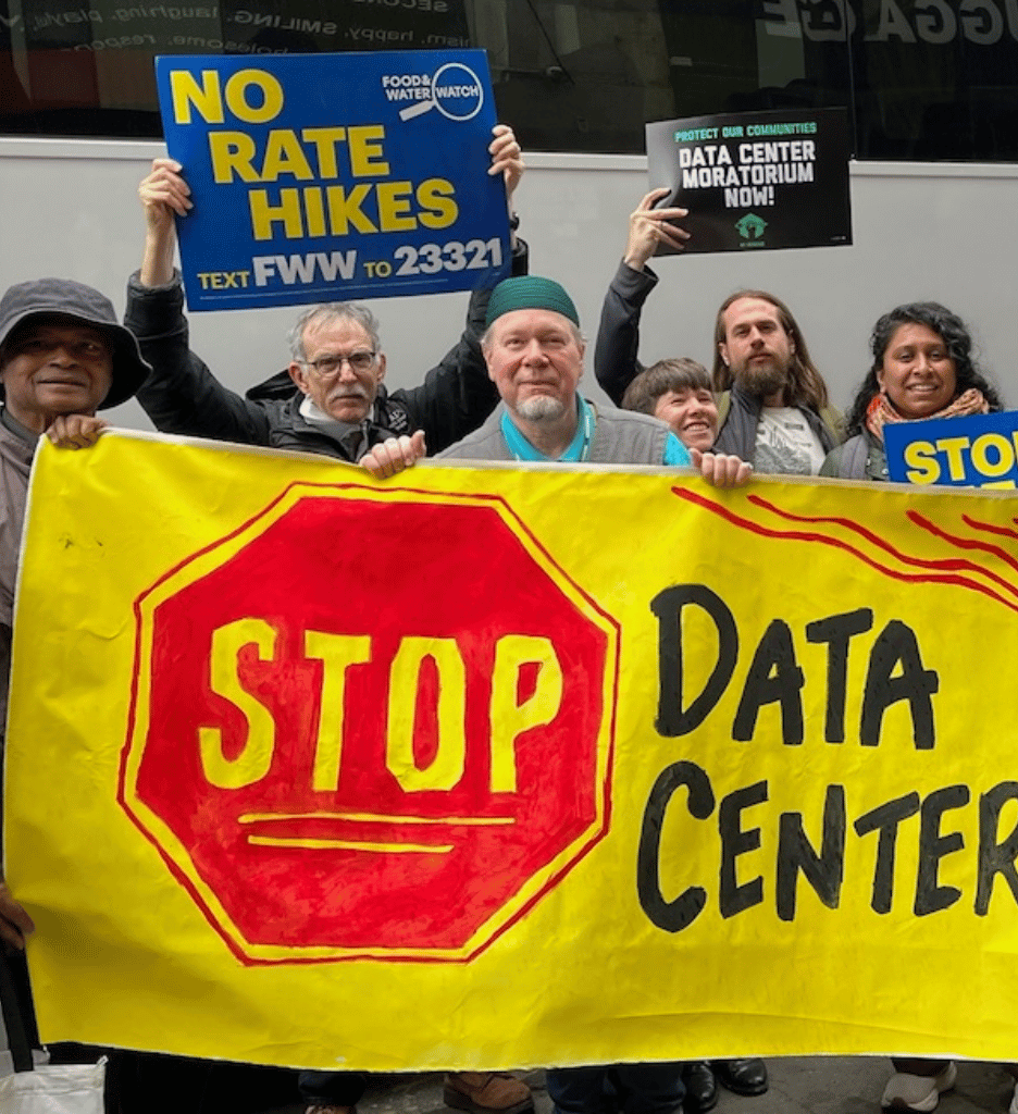 Handpainted yellow banner with a red stop sign and the message Stop Data Centers, held by a variety of activists holding signs to ask for a data center moratorium.
